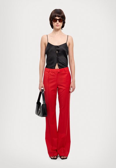 Black satin tank top with front buttons, red high-waisted wide-leg trousers, black handbag, and sunglasses. Smooth fabric and tailored fit.