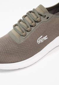 Baskets marron clair en tissu mesh avec un design texturé. Elles possèdent des lacets gris, un bout renforcé uni et une semelle en caoutchouc blanche.