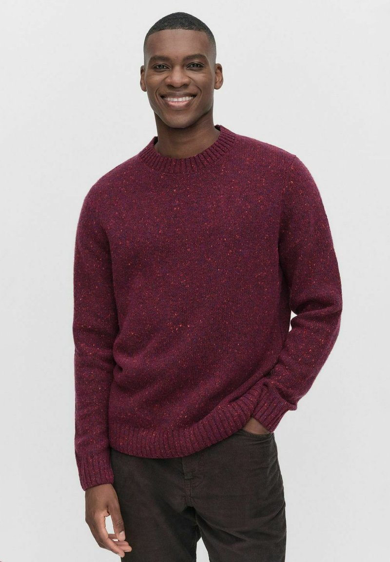 Bordeaux gebreide trui met een ronde halslijn en geribde manchetten. De stof heeft een gestructureerde textuur en subtiele kleurvariaties.