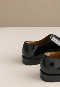 Sorte blanke lædersko med en glat tekstur, traditionelt snøredesign og lav stakket hæl, med en brun læderinderside.