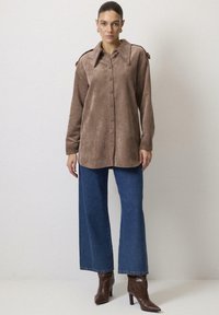 Brun corduroy skjortejakke med krave, frontknapper og skulderdetaljer. Kombineret med blå wide-leg jeans og brune hælede støvler.