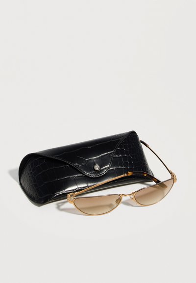 Λεπτά γυαλιά ηλίου με χρυσό σκελετό και καφετί φακούς με διαβάθμιση, τοποθετημένα μπροστά σε μαύρη υφασμάτινη δερμάτινη θήκη για γυαλιά με κούμπωμα.