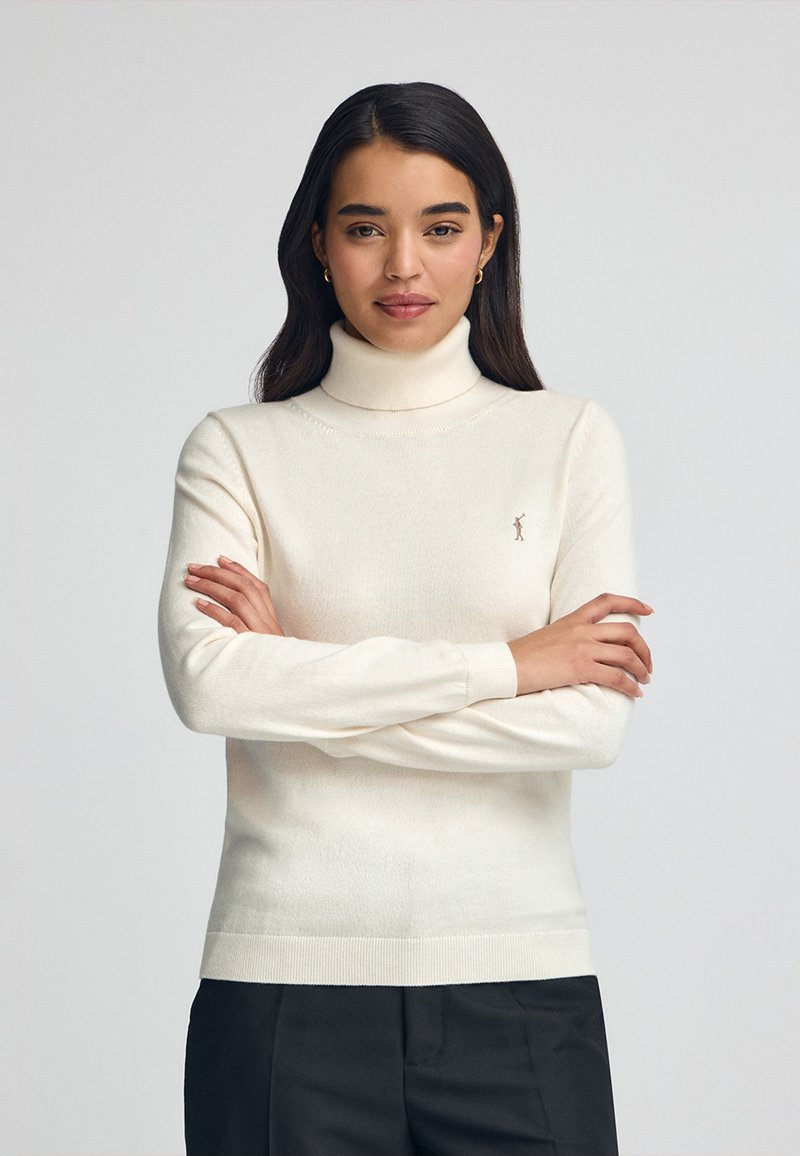 Maglione a colletto alto crema realizzato in morbido tessuto a maglia. Caratterizzato da maniche lunghe, polsini a coste e un piccolo logo sul petto. Design semplice e classico.