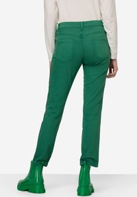 Zielone dżinsy o wysokim stanie, z dwiema tylnymi kieszeniami i zwężającym się krojem nogawek. W połączeniu z połyskującymi zielonymi botkami do kostki.