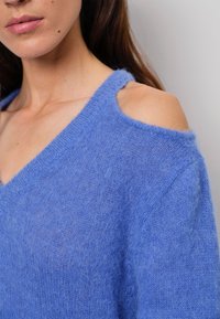 Leichter blauer Pullover mit einer weichen, strukturierten Oberfläche, ausgestattet mit einem tiefen V-Ausschnitt und einem schulterfreien Design.
