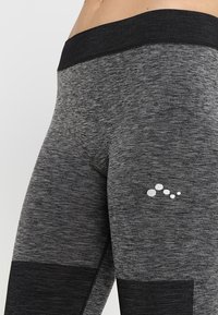 Szare legginsy sportowe z czarnym pasem, z teksturowanym, melanżowym wzorem oraz małym białym logo z boku.