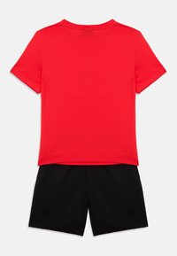 Rdeča majica s kratkimi rokavi in okroglim izrezom, kombinirana s črnimi kratkimi hlačami. Obe kosu sta izdelani iz mehkega blaga in imata klasičen priložnostni dizajn.