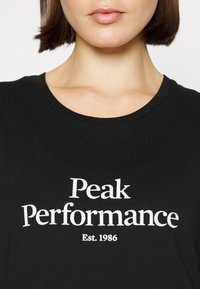 Černé bavlněné tričko s kulatým výstřihem, na přední straně s bílým nápisem "Peak Performance" a "Est. 1986".