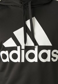 Czarna bluza z kapturem z dużym, białym logo Adidas. Materiał jest gładki o matowym wykończeniu. Zawiera sznurki z metalowymi końcówkami.