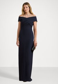 Tengerészkék, váll nélküli ruha, testhez simuló fazonban, a szoknya részén drapírozással, egyenes sziluettel, melyet egy fekete clutch táska egészít ki.