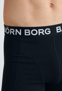 Schwarze Boxerbriefs mit einem breiten elastischen Bund, auf dem der Markenname "BJÖRN BORG" in Weiß steht. Glatte Textur mit figurbetontem Schnitt.