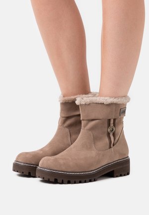 Tan suede ankle boots with a faux fur cuff, decorative stitching, side logo detail, and a textured rubber sole.
