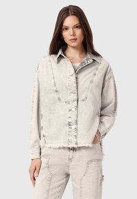 Jasnoszara kurtka dżinsowa o lekko skróconym kroju, z widocznym przeszyciem i postrzępionym dołem. Posiada duże kieszenie i srebrne zatrzaski.