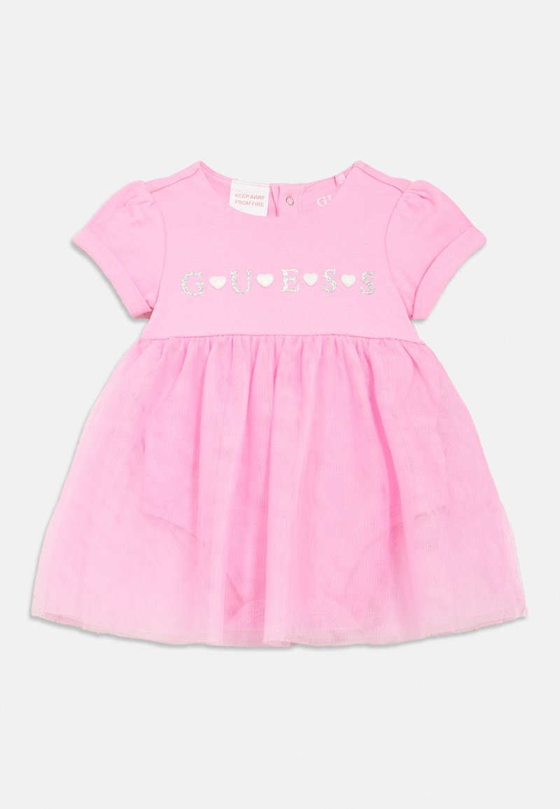 Ροζ βρεφικό φόρεμα με βαμβακερό τοπ και τούλινη φούστα. Στο μπροστινό μέρος υπάρχει ασημί κείμενο "GUESS" με καρδιές. Κοντά μανίκια με φούσκες, κλείσιμο με κουμπί στο λαιμό.