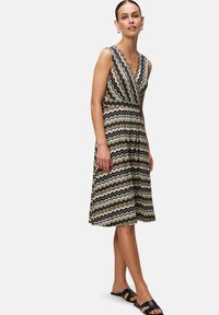 Gemêleerd jurk met een V-hals, mouwloos ontwerp en een elastische taille. Kleuren zijn zwart, goud en room in een zigzagpatroon.