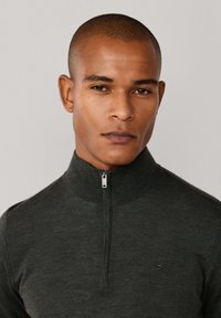 Dunkelgrüner Reißverschluss-Pullover aus weichem Stoff, mit einem hohen Kragen, subtiler Logo auf der Brust und einer taillierten Passform.