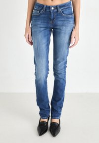 Jeans en denim bleu skinny avec un lavage décoloré, design à cinq poches et fermeture à bouton. Associés à des chaussures noires à bout pointu.