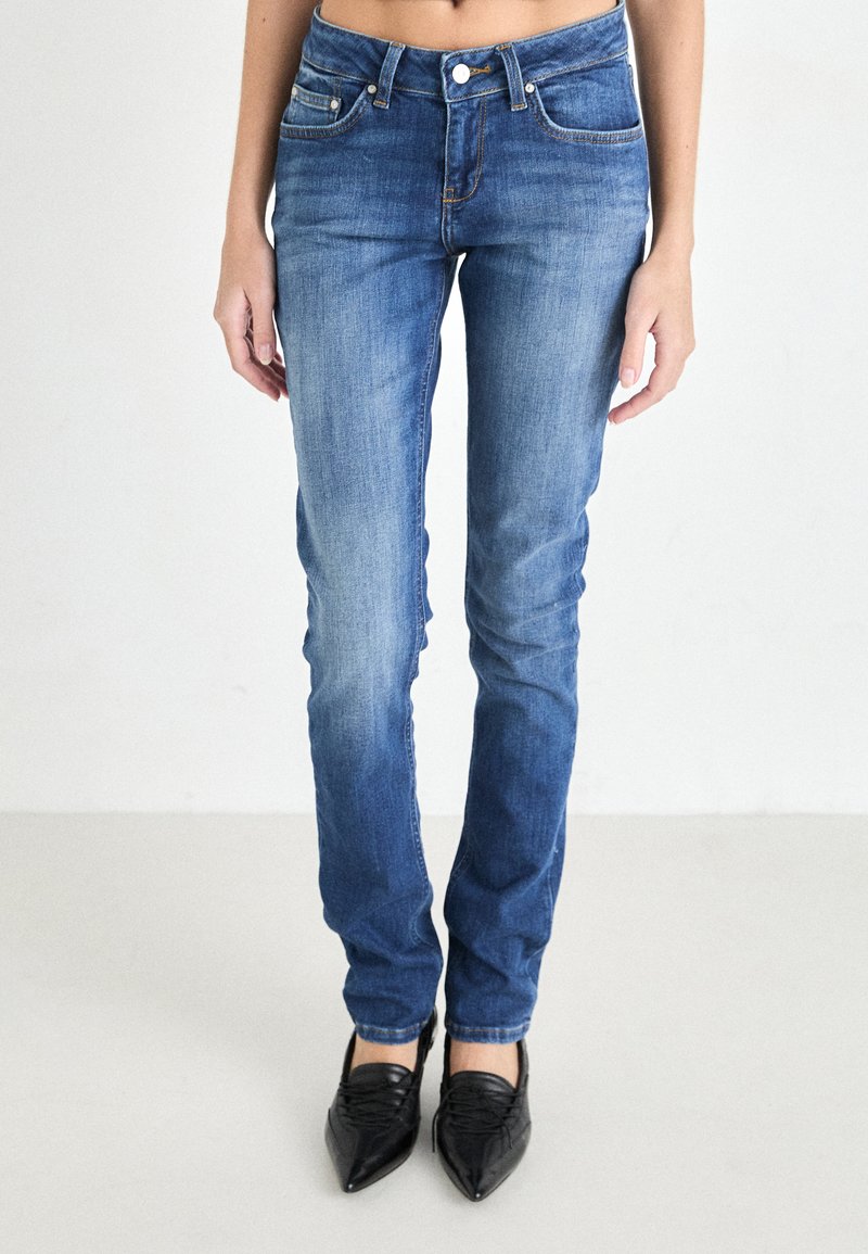 Jeans en denim bleu skinny avec un lavage décoloré, design à cinq poches et fermeture à bouton. Associés à des chaussures noires à bout pointu.