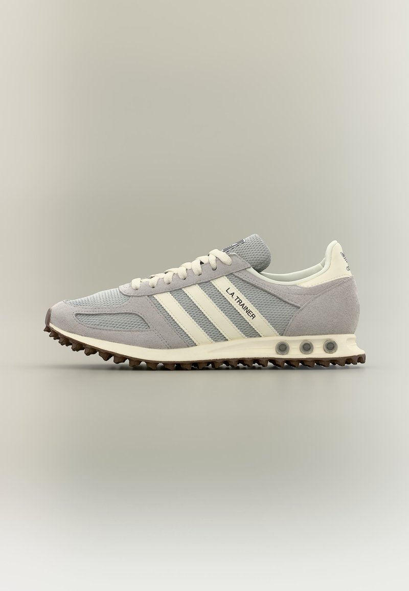 Baskets Adidas L.A. Trainer gris clair avec des bandes blanches, dessus en mesh texturé et semelle cloutée marron sur fond neutre.
