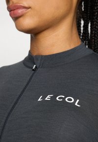 Mørkegrå sykkeltrøye med glidelåskrage og hvit "LE COL"-logo på brystet. Stoffet har en teksturert overflate.