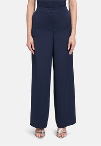 Pantalons larges bleu marine en tissu lisse avec une taille ajustée et un design sans coutures, associés à des talons aiguilles argentés à lanières.