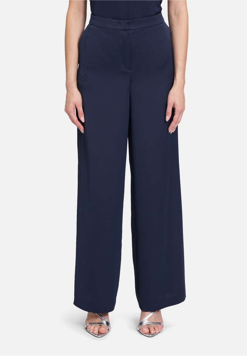 Pantalons larges bleu marine en tissu lisse avec une taille ajustée et un design sans coutures, associés à des talons aiguilles argentés à lanières.