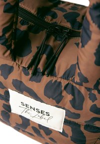 Braune, gepolsterte Tasche mit dunklem Tiermuster. Schwarzer Reißverschluss und Kordeln sind vorhanden. Das Etikett trägt die Aufschrift "SENSES The Label" in Weiß.