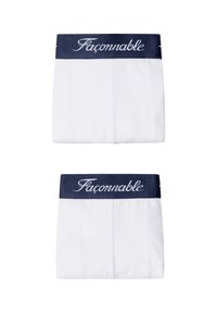 Dos bóxers blancos doblados con cinturillas azul marino que presentan el nombre de la marca "Façonnable" en letra blanca cursiva.