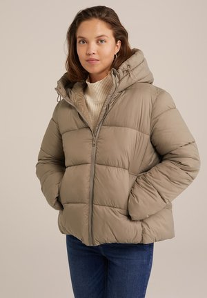Puffer jacket in light beige with a hood, featuring a zip closure and quilted pattern. Worn over a textured cream sweater and blue jeans.