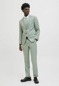 Completo verde chiaro realizzato in tessuto liscio, dotato di giacca monopetto e pantaloni su misura, abbinato a una cravatta coordinata e scarpe nere.