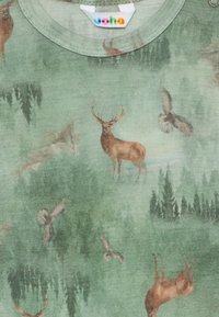 Žalias medvilnės marškinėliai su gamtos tema, kurioje pavaizduoti elniai ir pelėdos tarp medžių, minkšta tekstūra, apvalus iškirpimas, matoma etikėtė.