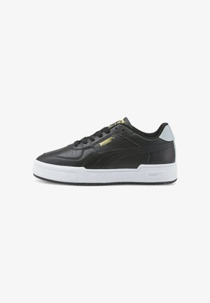 Zapatilla negra de perfil bajo Puma con suela blanca, logo dorado de Puma en el lateral y lengüeta blanca en el talón, mostrada en perfil lateral.