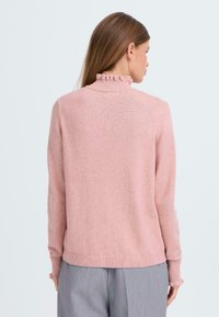 Pull en tricot rose avec un col froncé haut et des poignets côtelés, présentant une texture lisse et une coupe décontractée. La vue de dos est montrée.