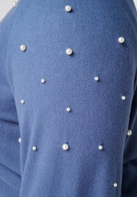 Blauwe stof met kleine en middelgrote witte parelversieringen verspreid over het oppervlak.