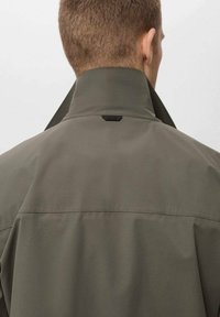 Dunkelgrüne Jacke mit hohem Kragen und matter Oberfläche. Verfügt über ein kleines Logo-Detail auf der Rückseite, eine glatte Textur und ein strukturiertes Design.