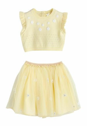 Żółty dziergany top bez rękawów z białymi aplikacjami kwiatowymi oraz dopasowana żółta spódnica tiulowa z kwiatowym haftem.