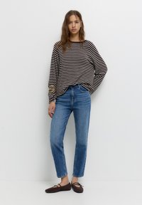 Gestreifte Langarmbluse in Braun und Creme, kombiniert mit hellblauen geraden Jeans. Braune Ballerinas mit Bindeband vorne.