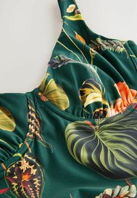 Groen bloemenbadpak met grote, getextureerde bladeren en levendige bloemen, met geplooide stof rond de halslijn voor extra dimensie.