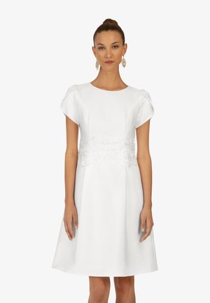 Robe blanche courte avec de courtes manches volumineuses, corsage ajusté et détails en dentelle à la taille. Tissu lisse, ourlet au genou.