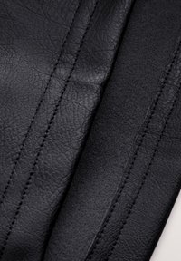 Pelle nera con finitura testurizzata, cuciture visibili e una striscia di accento liscia. Il tessuto contrasta con una sezione opaca.