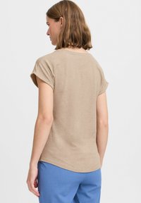 T-shirt beige a maniche corte in tessuto morbido, con scollo rotondo e orlo curvo, abbinato a pantaloni azzurri chiari.