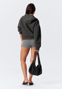 Gray hoodie with a relaxed fit and hood, paired with gray shorts. Black handbag with studs and open-toed black heels completes the look.