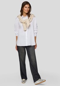 White button-up shirt, oversized fit, rolled sleeves, paired with dark wide-leg jeans and a light beige knit scarf draped around the neck.
