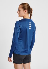 Mörkblå långärmad träningströja med rund halsringning och vit chevron-design på baksidan, i kombination med svarta shorts. Slät textur.