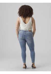 Light beige ribbed tank top, denim skinny jeans in light blue, ankle-strap heels, smooth texture, and fitted design accentuating shape.
