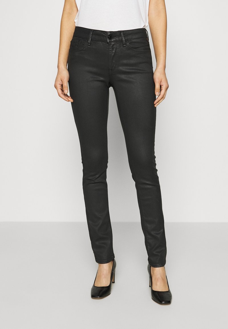 Jeans ajustados negros con un diseño entallado, hechos de tela vaquera, que presentan una cintura alta y un cierre de botón. Llevados con tacones negros.