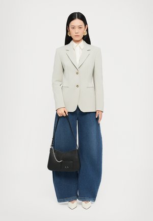 Blazer gris clair à deux boutons, associé à une chemise blanche rayée, un jean large en denim foncé et un sac à main noir avec des détails en chaîne argentée.