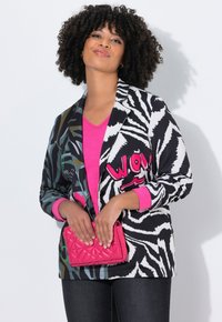 Blazer a strisce zebrate in bianco e nero con dettagli rosa, abbinato a un top a V rosa. Tiene una borsa rosa trapuntata. Jeans scuri.