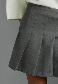 Jupe mini plissée grise en matériau doux, avec plusieurs plis et un ourlet soigné, associée à un pull en tricot de couleur claire.