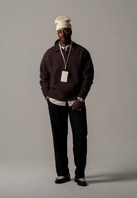 Suéter texturizado de gran tamaño en color púrpura oscuro, camisa blanca con cuello debajo, pantalones negros, gorro de punto blanco y mocasines negros. Cordón con tarjeta.